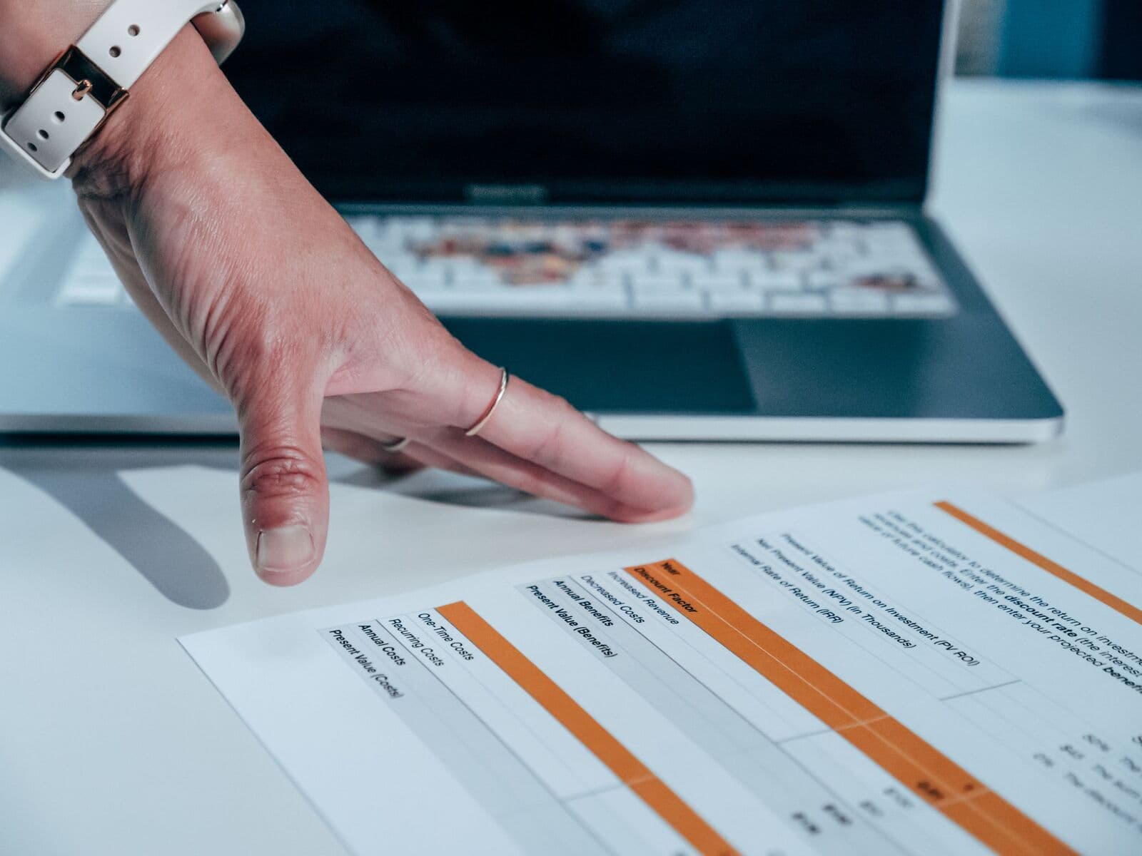 Hand auf einem ausgedruckten Bericht mit markierten Tabellenzeilen neben einem Laptop